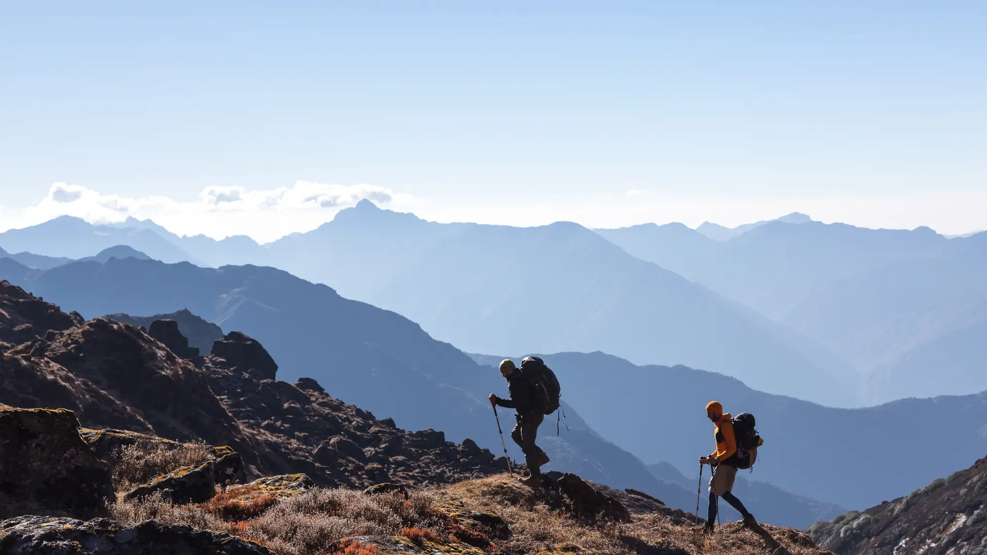 Zwei Wanderer mit Trekkingstöcken auf einem Bergrücken vor Alpenpanorama